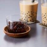 A cup of cooked tapioca pearls with milk tea drinks next to it.