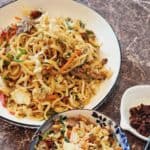 A plate of Cantonese beef chow mein with chilli oil next to it.