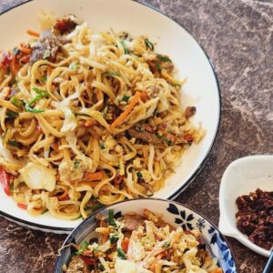 A plate of Cantonese beef chow mein with chilli oil next to it.