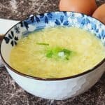 A bowl of egg drop soup with green onion in it.