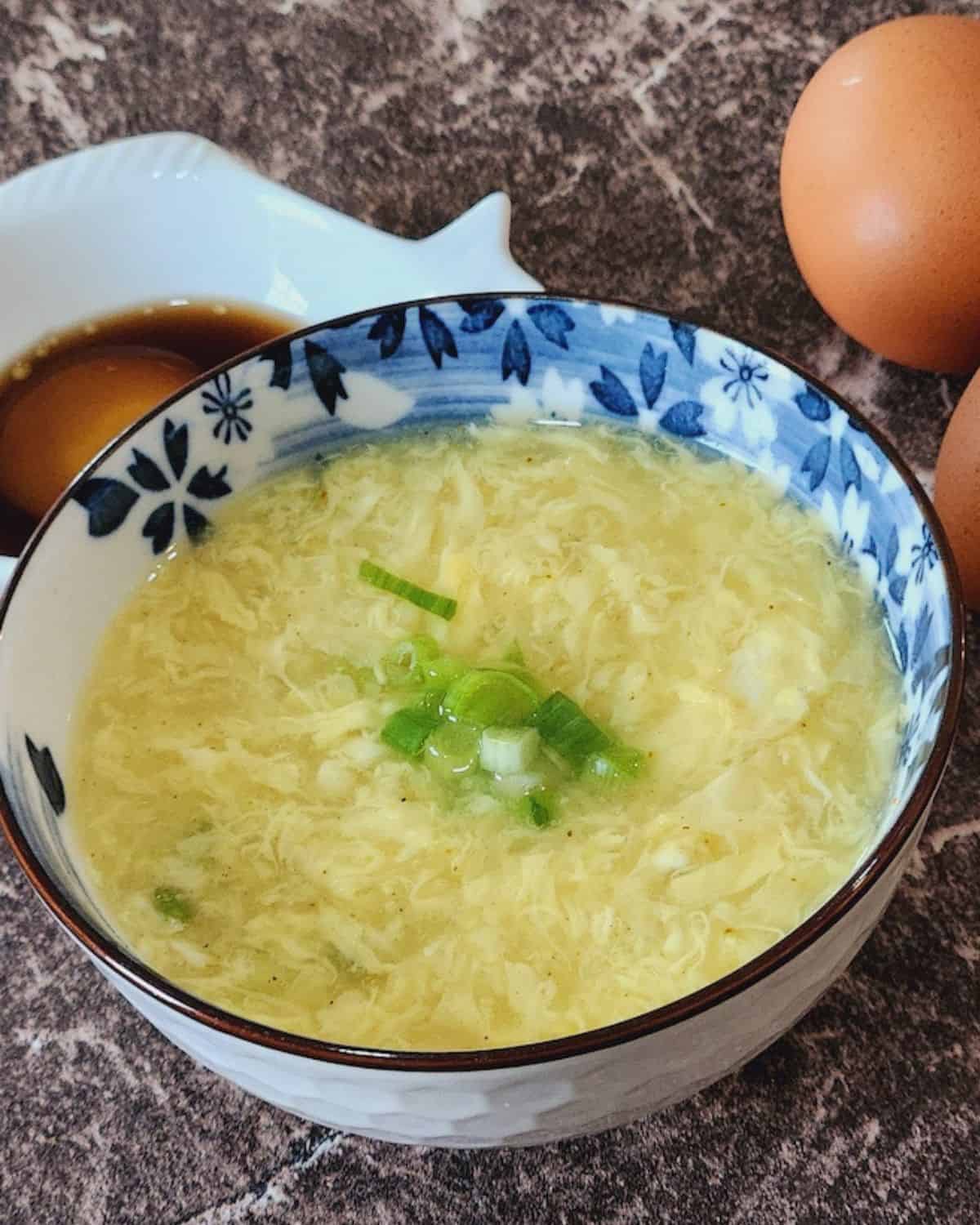 A bowl of egg drop soup with green onion in it.