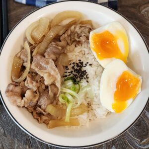 A photo of Yoshinoya gyudon beef on fluffy white rice and a soft-boiled egg cut in half.