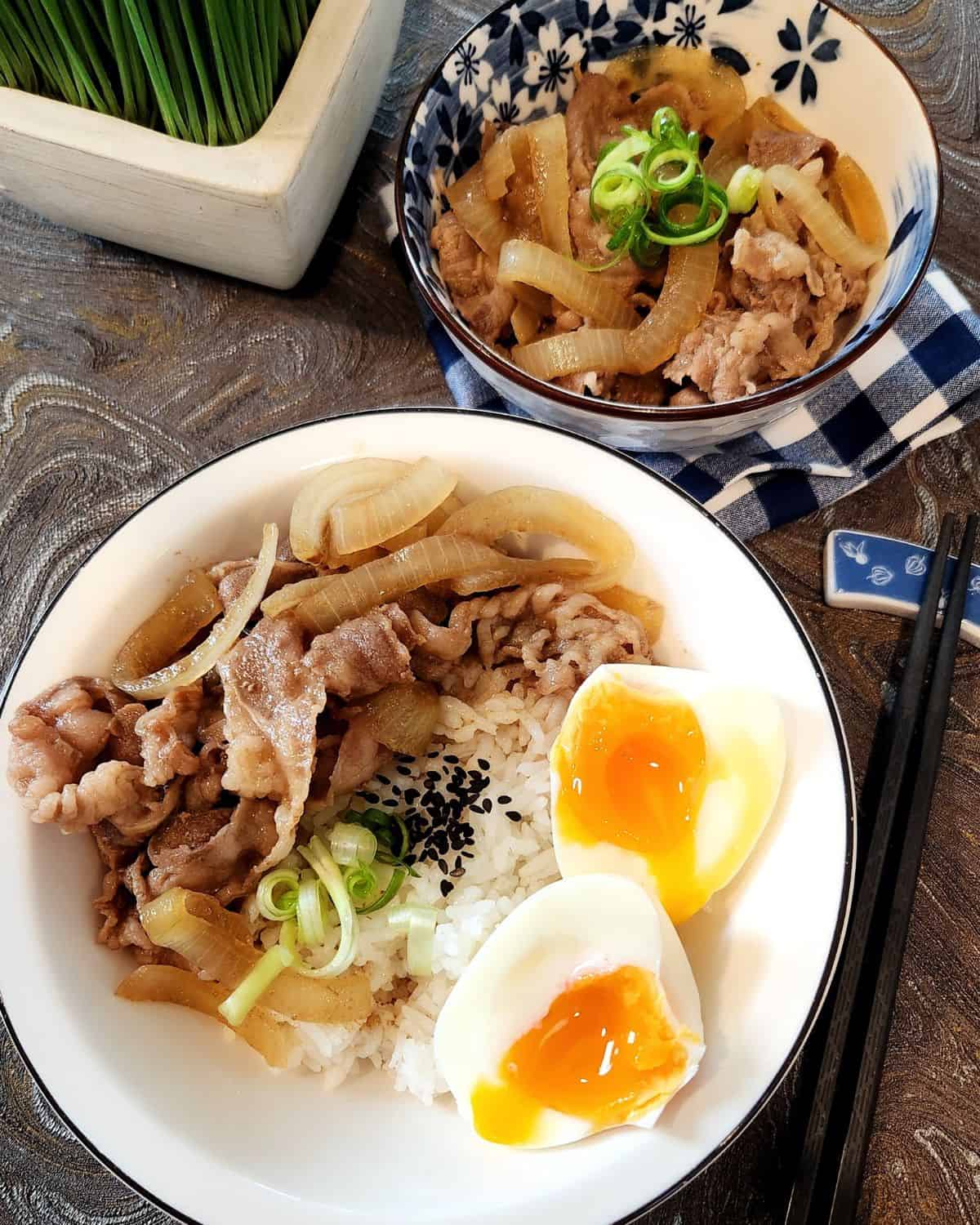 A bowl of Yoshinoya gyudon beef with soft-boiled egg and another small bowl of beef gyudon next to it.
