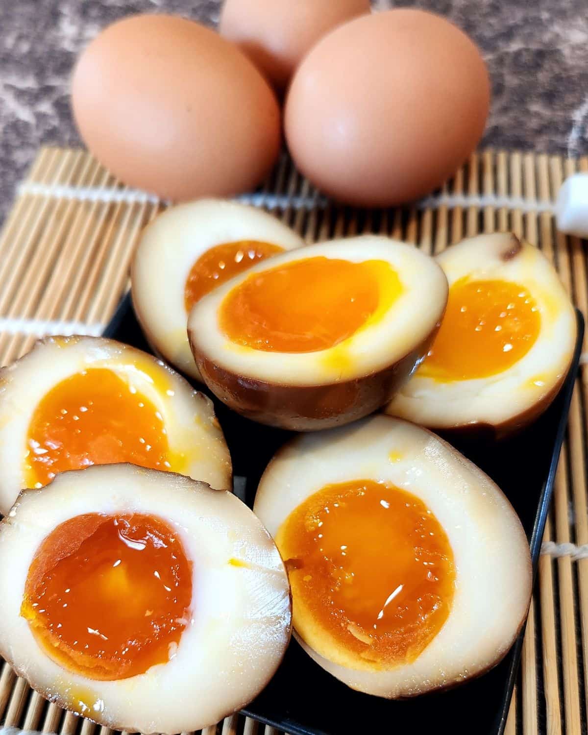 Ajitsuka tamago or ramen eggs cut in halves on bamboo tray.