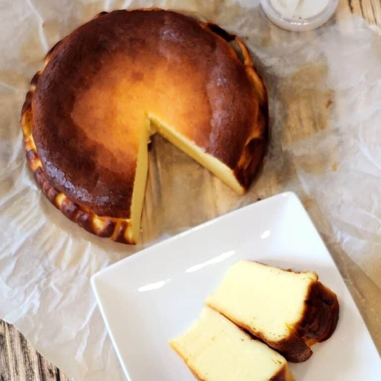 A photo of two slices of burnt basque cheesecake on a white, square plate and the rest on parchment paper.
