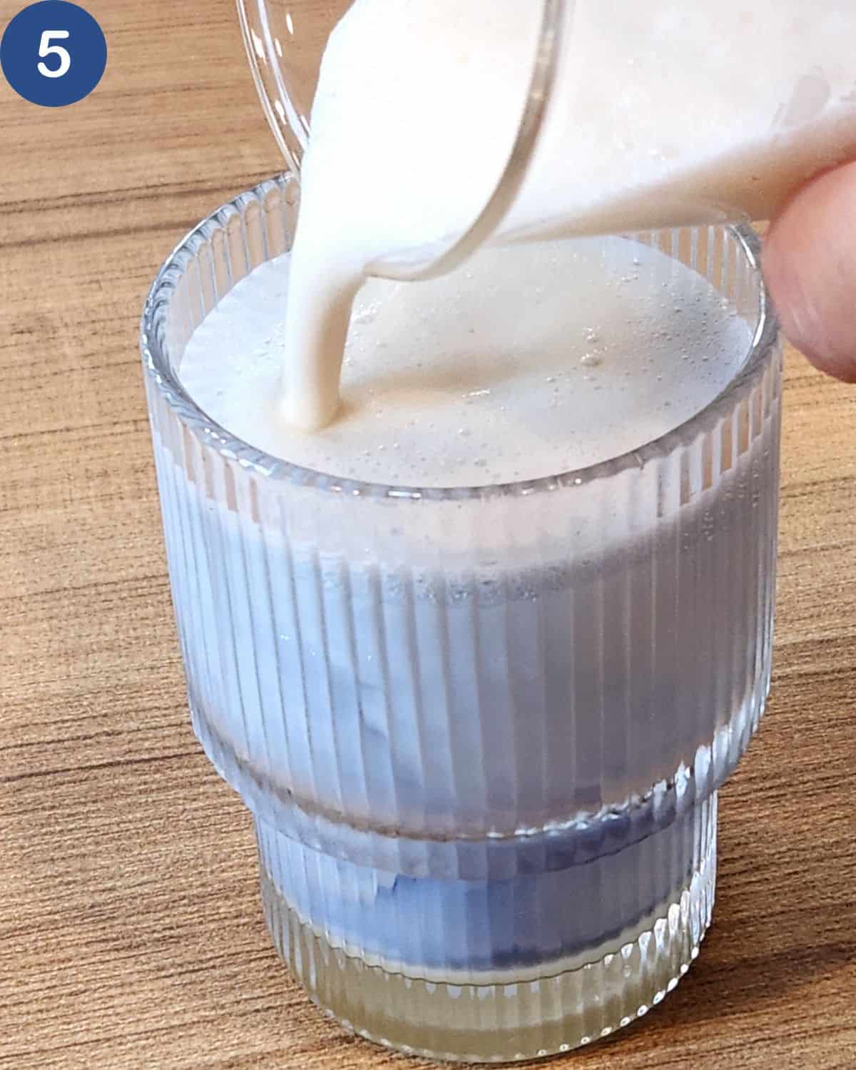 A photo of frothed milk poured into the butterfly pea flower tea in a glass.