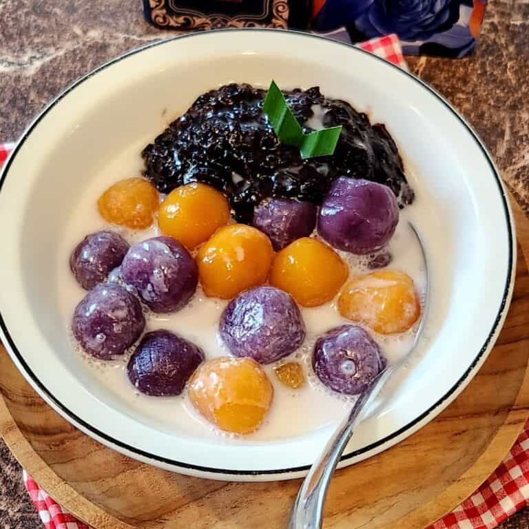 A bowl of candil ubi biji salak with coconut cream sauce on top of a wooden plate.