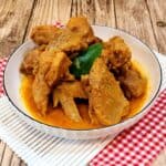 A picture of chicken rendang in a white plate on red white cloth.