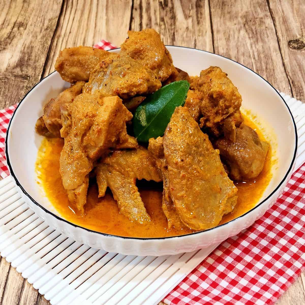 A picture of chicken rendang in a white plate on red white cloth.