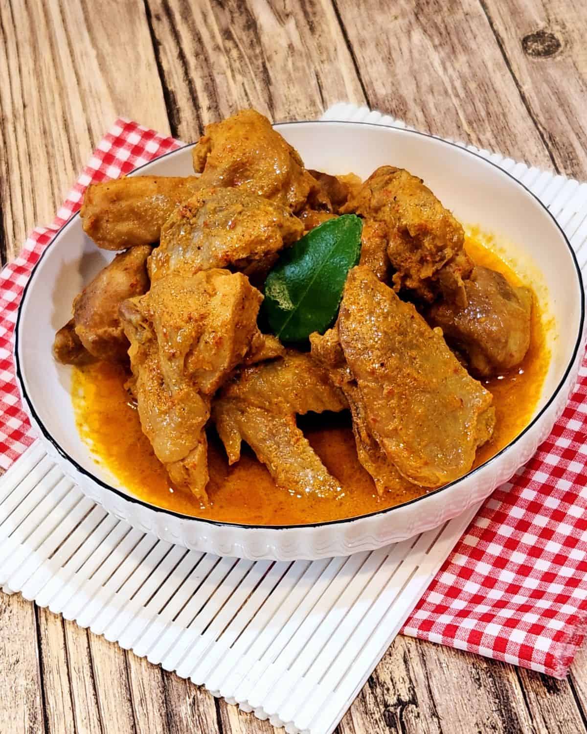 A plate of chicken rendang on white tray and red white cloth.