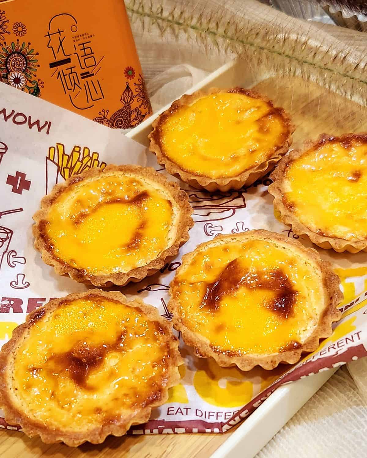 Five Hokkaido Cheese Tarts on a piece of paper and a wooden tray.