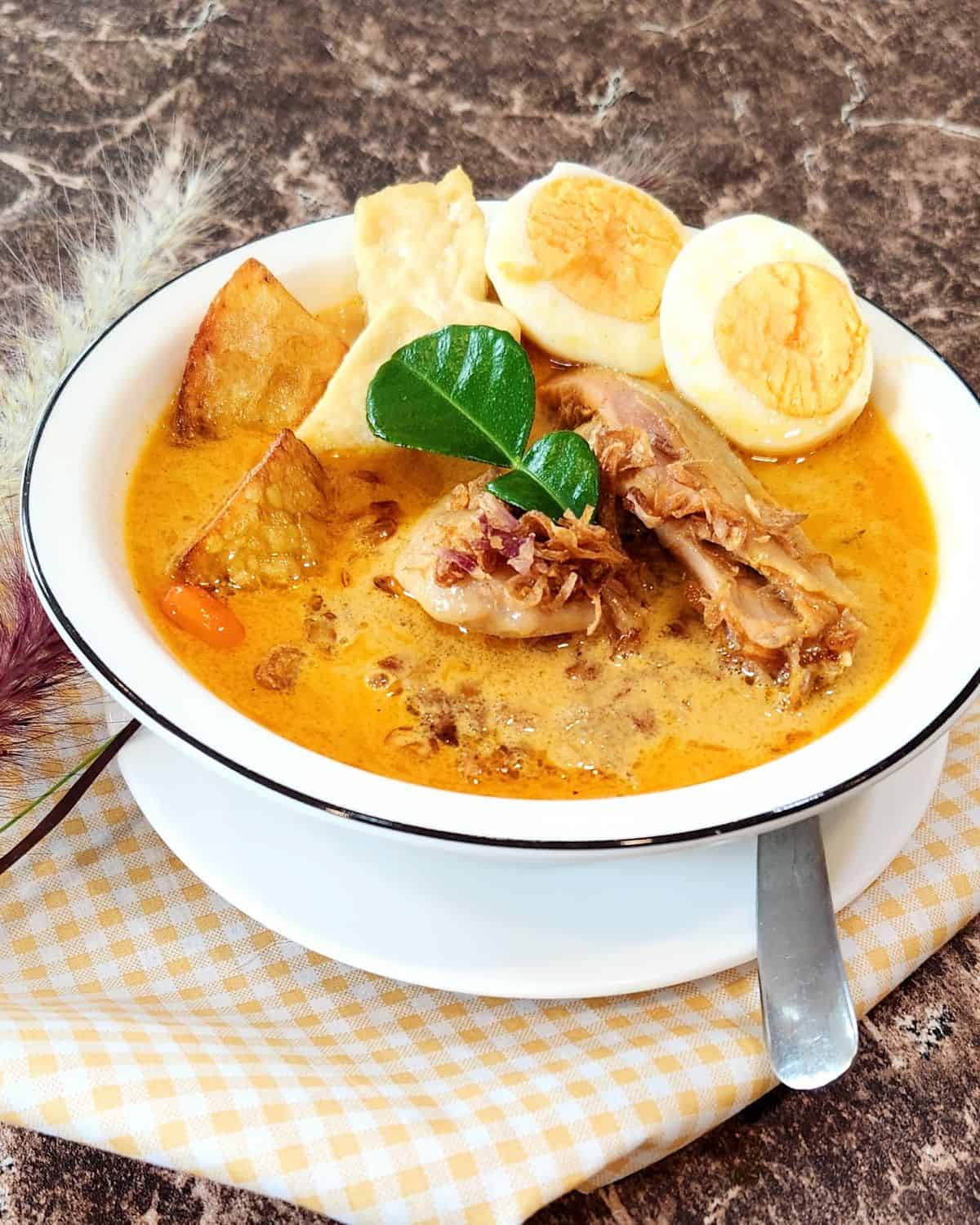 A bowl of Indonesian Kari Ayam with tofu, boiled egg, and fried potato, garnished with fried shallots.