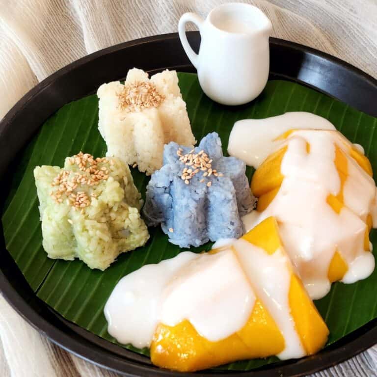 Thailand Mango Sticky Rice in three colors on a banana leaf with creamy coconut sauce.