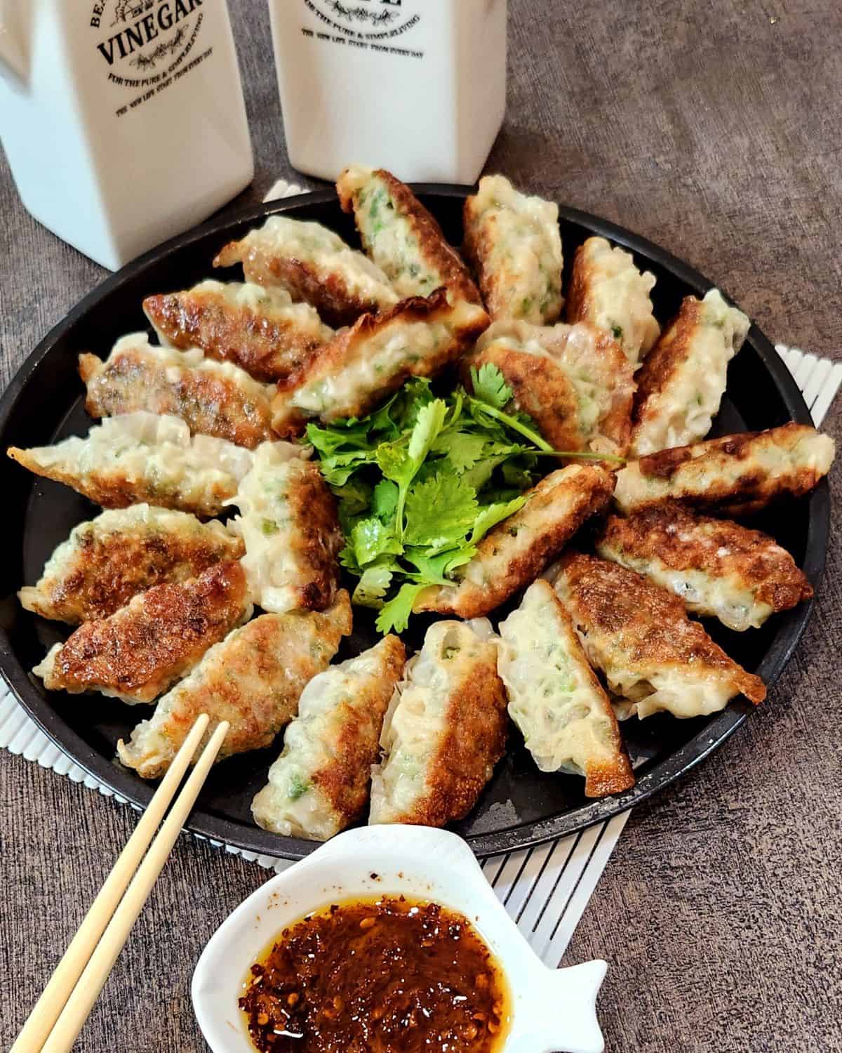 A photo of chicken potstickers lined on a round, black plate with coriander leaves in the center.