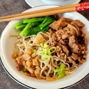 A bowl of minced pork noodles with vegetables and chopsticks.