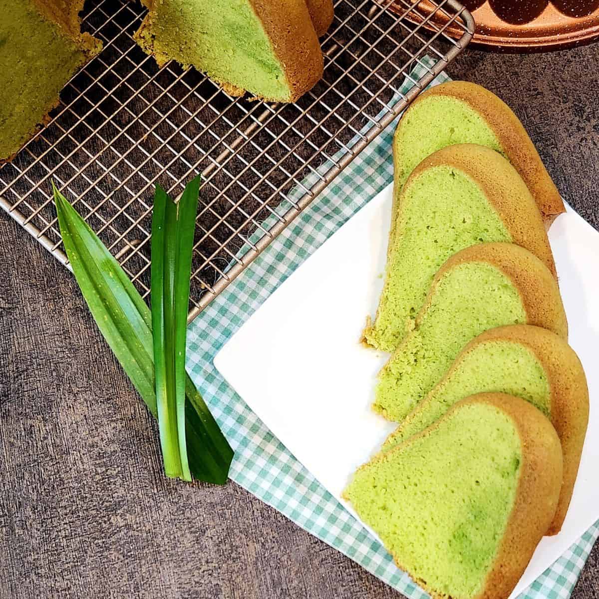 Pandan Cake slices on a white plate next to a few pandan leaves.