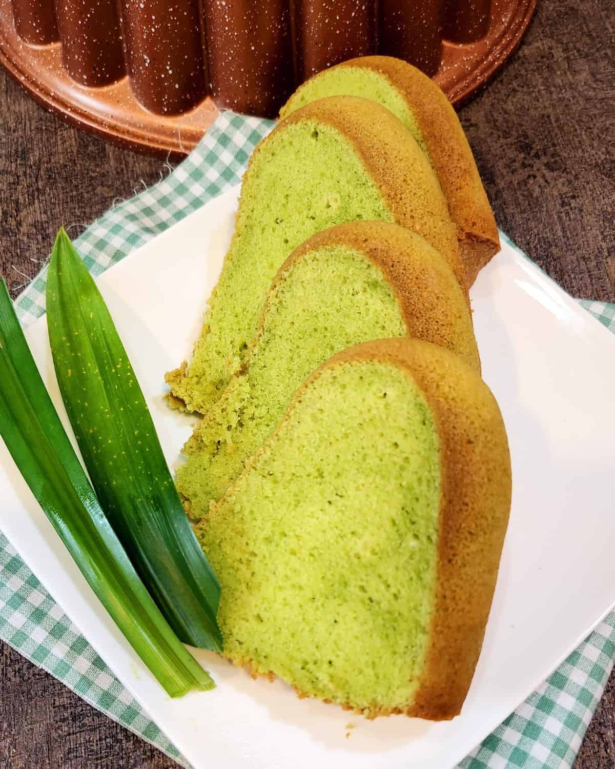 Pandan Cake slices on a white plate next to a few pandan leaves.