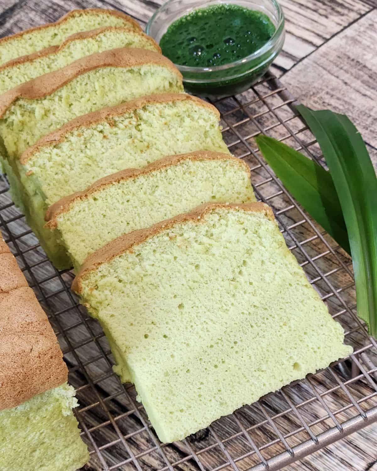 A few slices Taiwanese Castella Cake in pandan flavor on a cooling rack with pandan leaves next to it.
