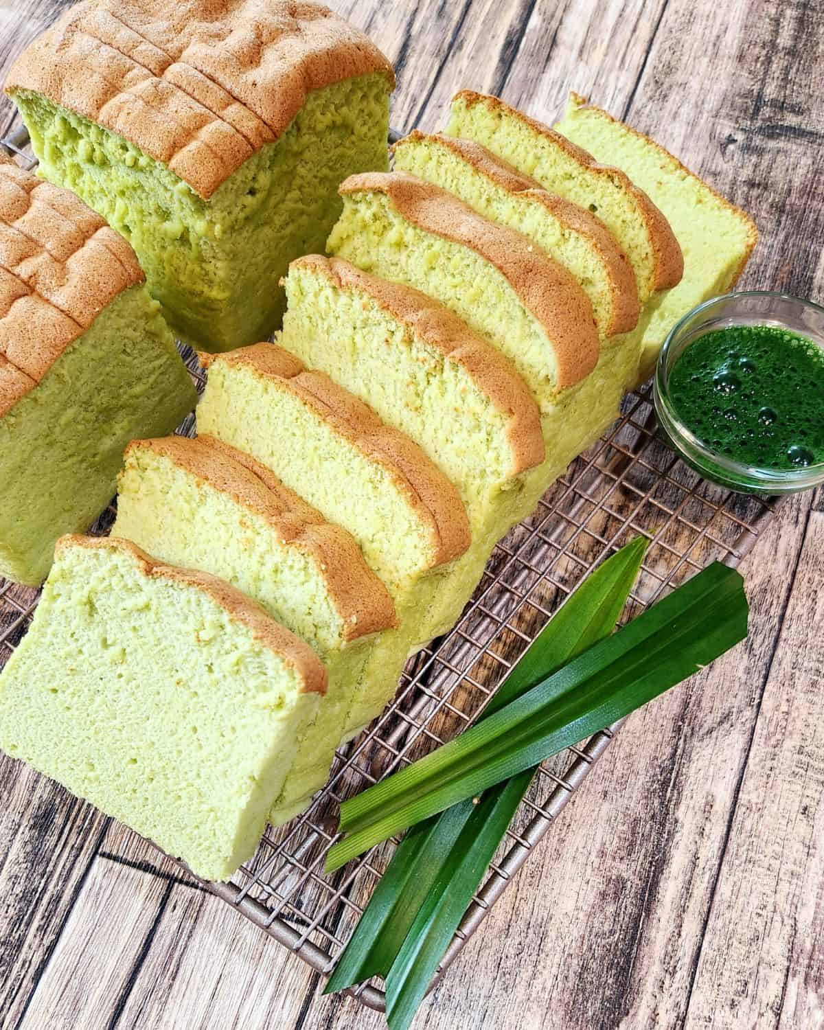 A few slices Taiwanese Castella Cake in pandan flavor on a cooling rack with pandan leaves next to it.