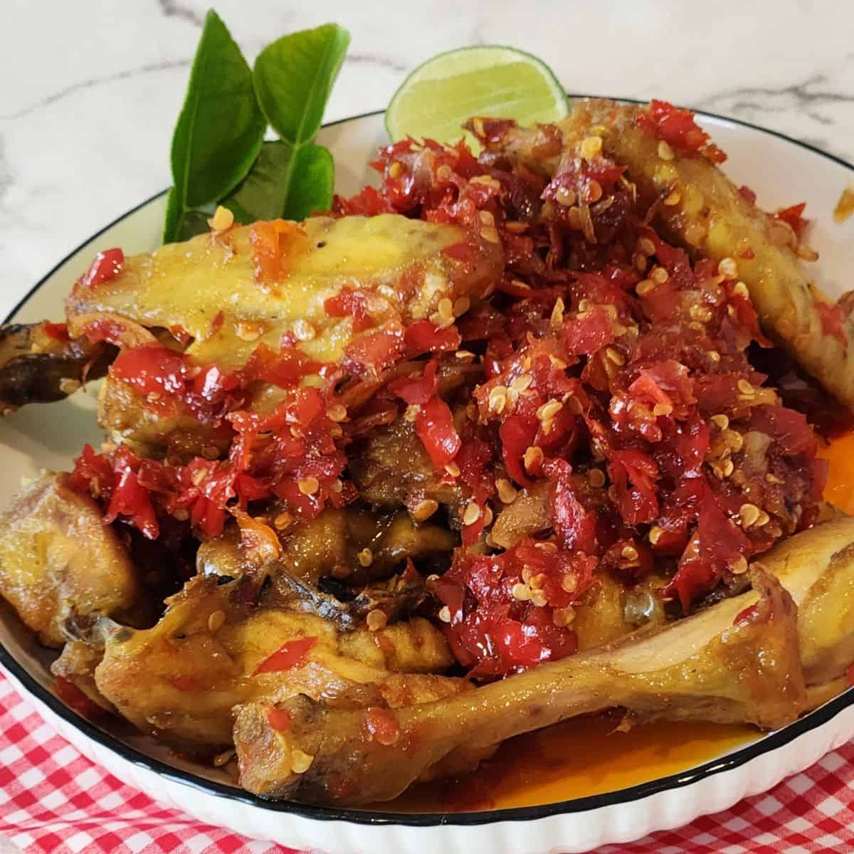 A plate of Ayam Balado garnished with lime leaves and a wedge of lime on red white cloth.