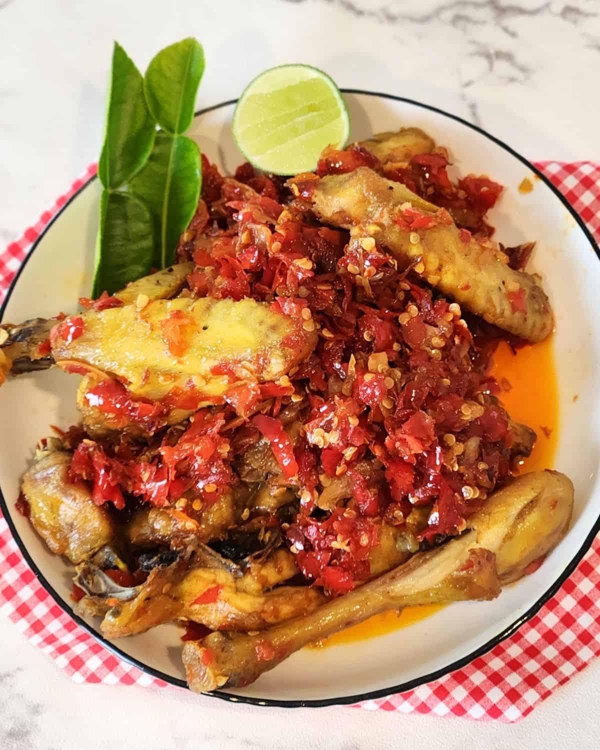 A plate of Ayam Balado garnished with lime leaves on a red white cloth.
