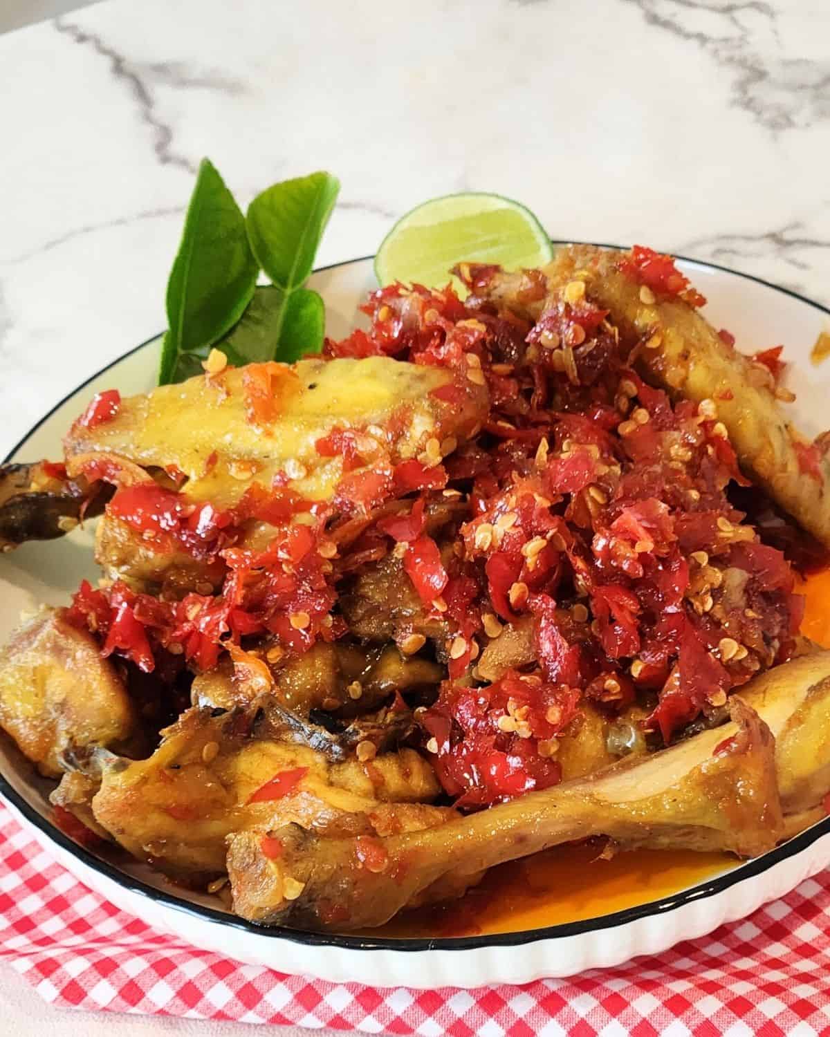 A plate of Ayam Balado with lime leaves and a wedge of lime.