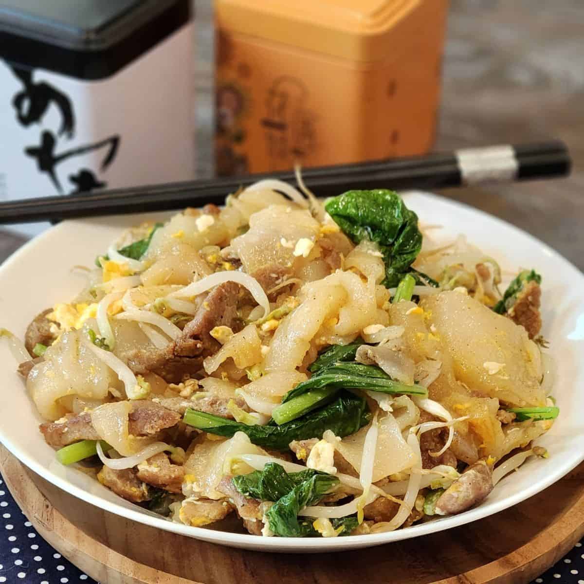 Beef Chow Fun or Kwetiau Goreng on a white plate with black chopsticks.