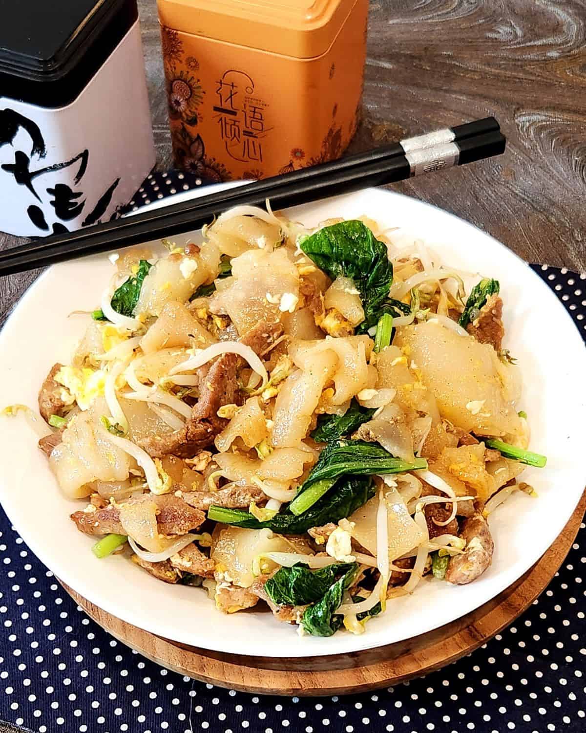 Beef Chow Fun or Kwetiau Goreng on a white plate with black chopsticks.