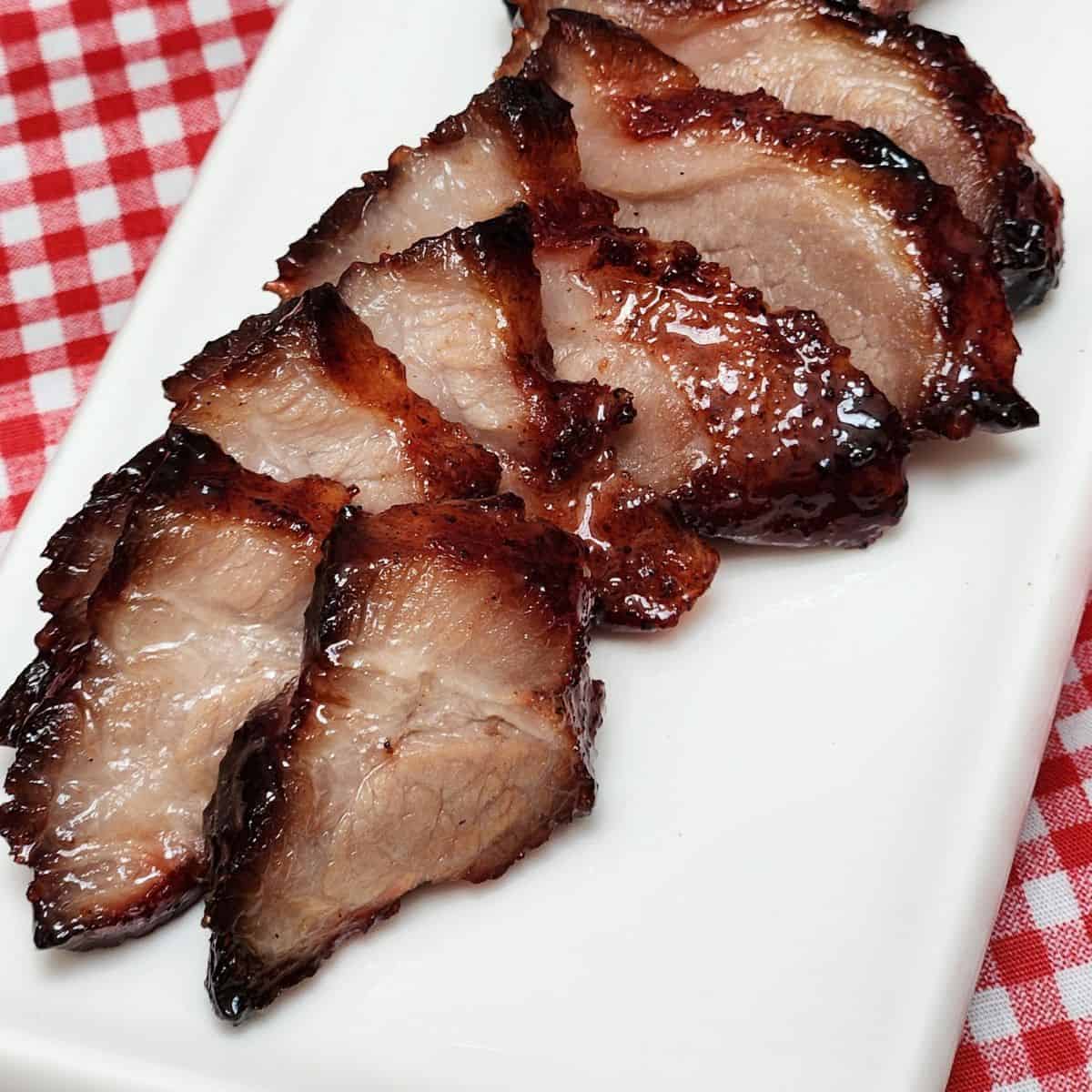 Char Siu Roast Pork slices on a long white plate on red white table cloth.