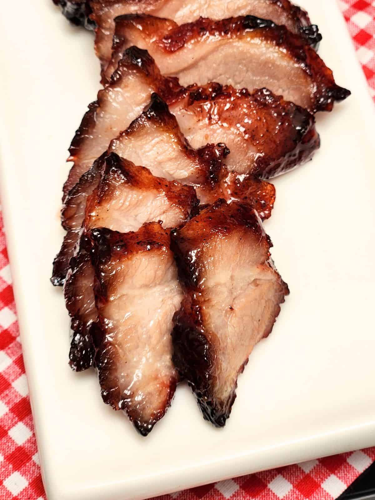 Char Siu Pork slices on a long white plate on red white table cloth.