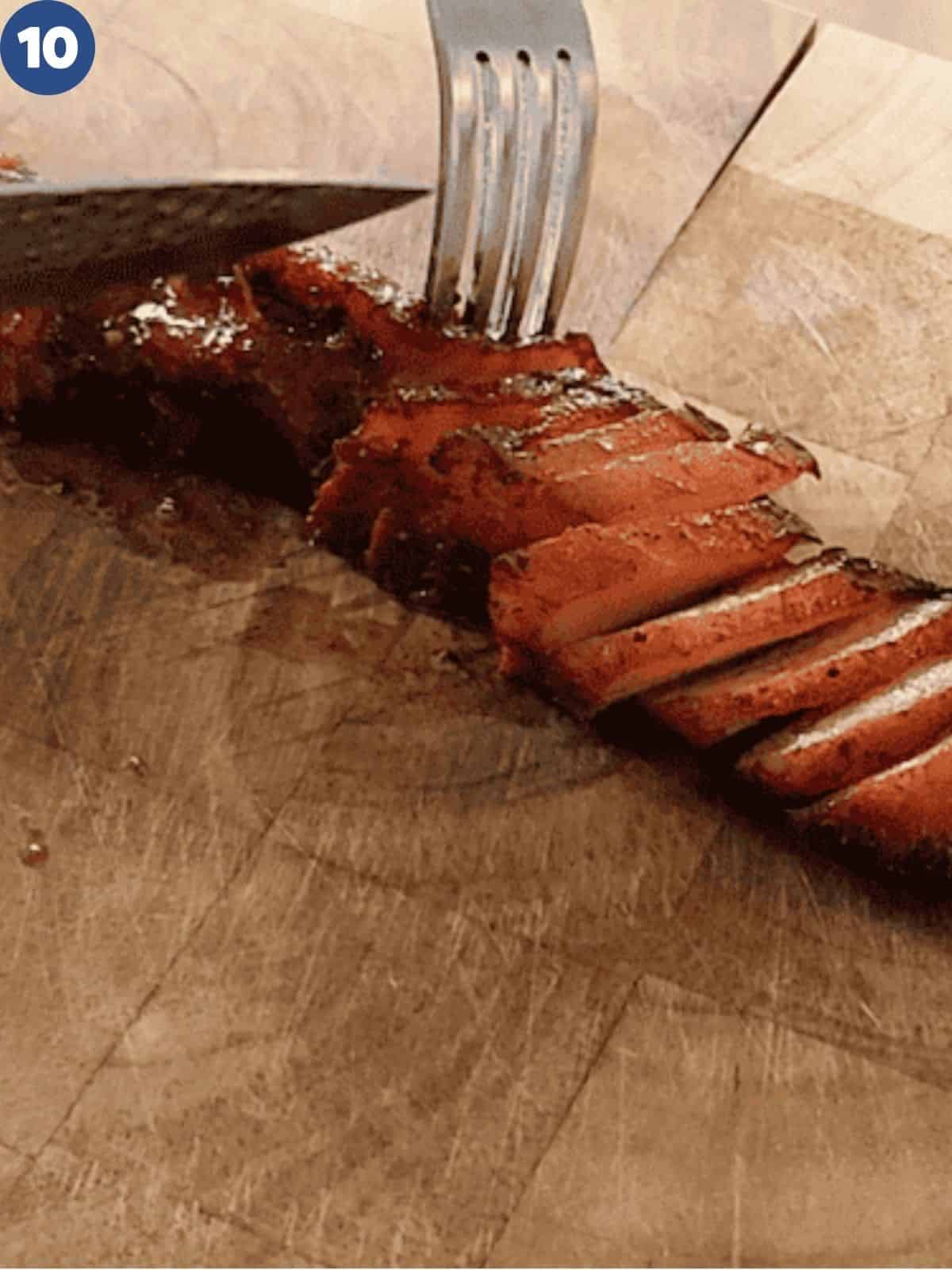 Char siu roast pork is being sliced on a wooden cutting board.