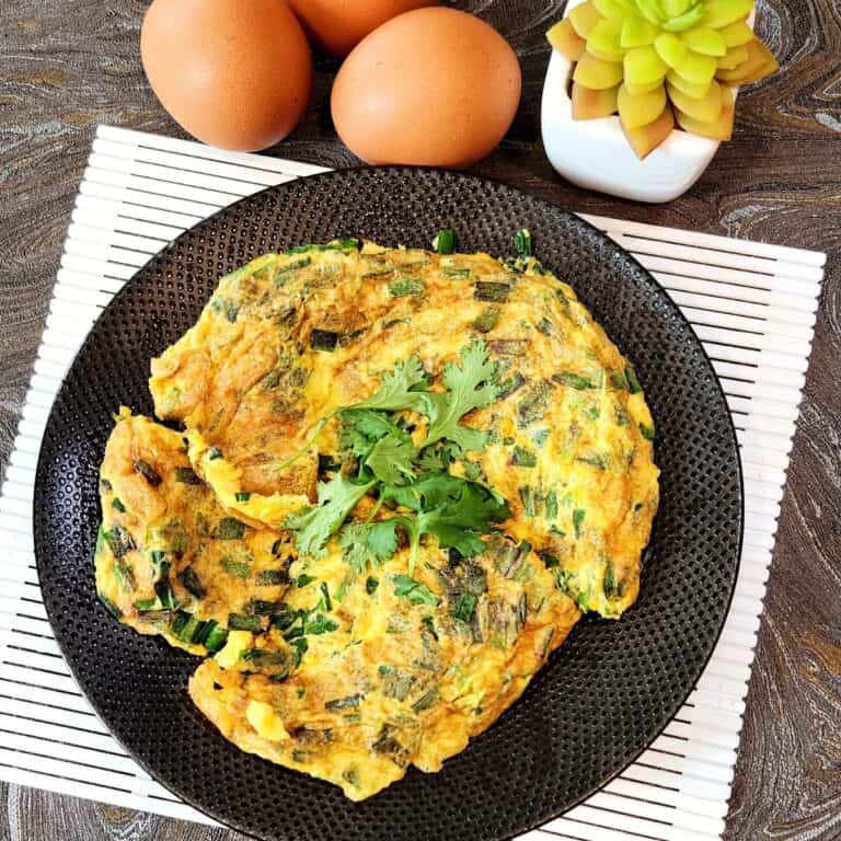 A black plate with Chinese chive eggs on top, garnished with coriander leaves.