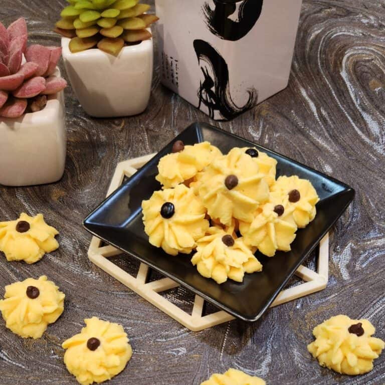 Custard cookies on a small, black plate with several cookies on granite table.