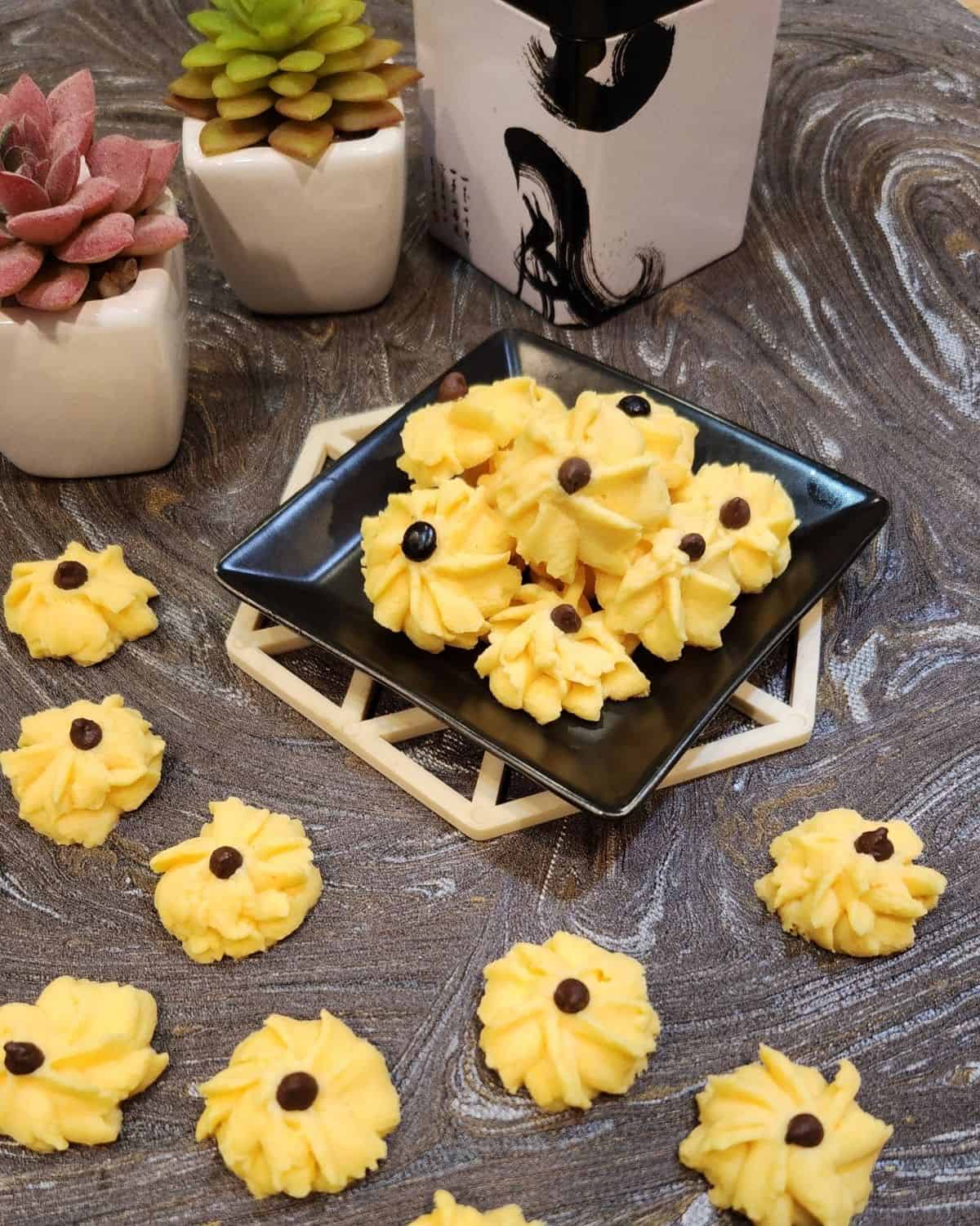 Custard cookies on a small, black plate with several cookies on granite table.