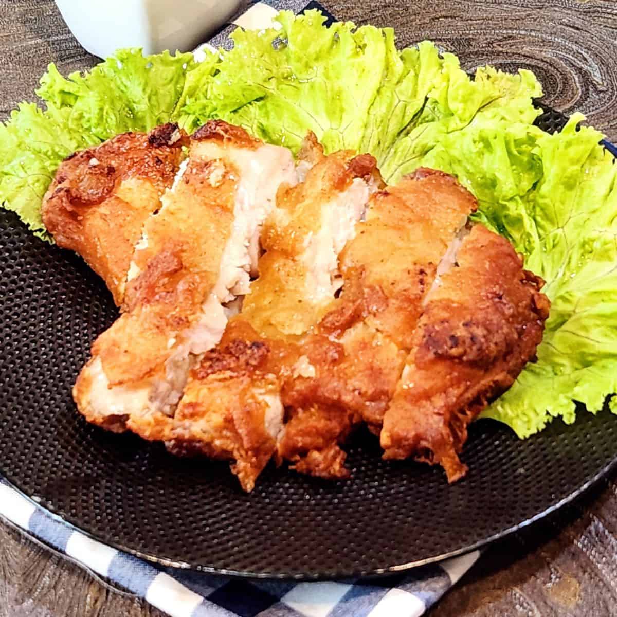 Gluten-free fried chicken slices on a black plate, garnished with lettuce.