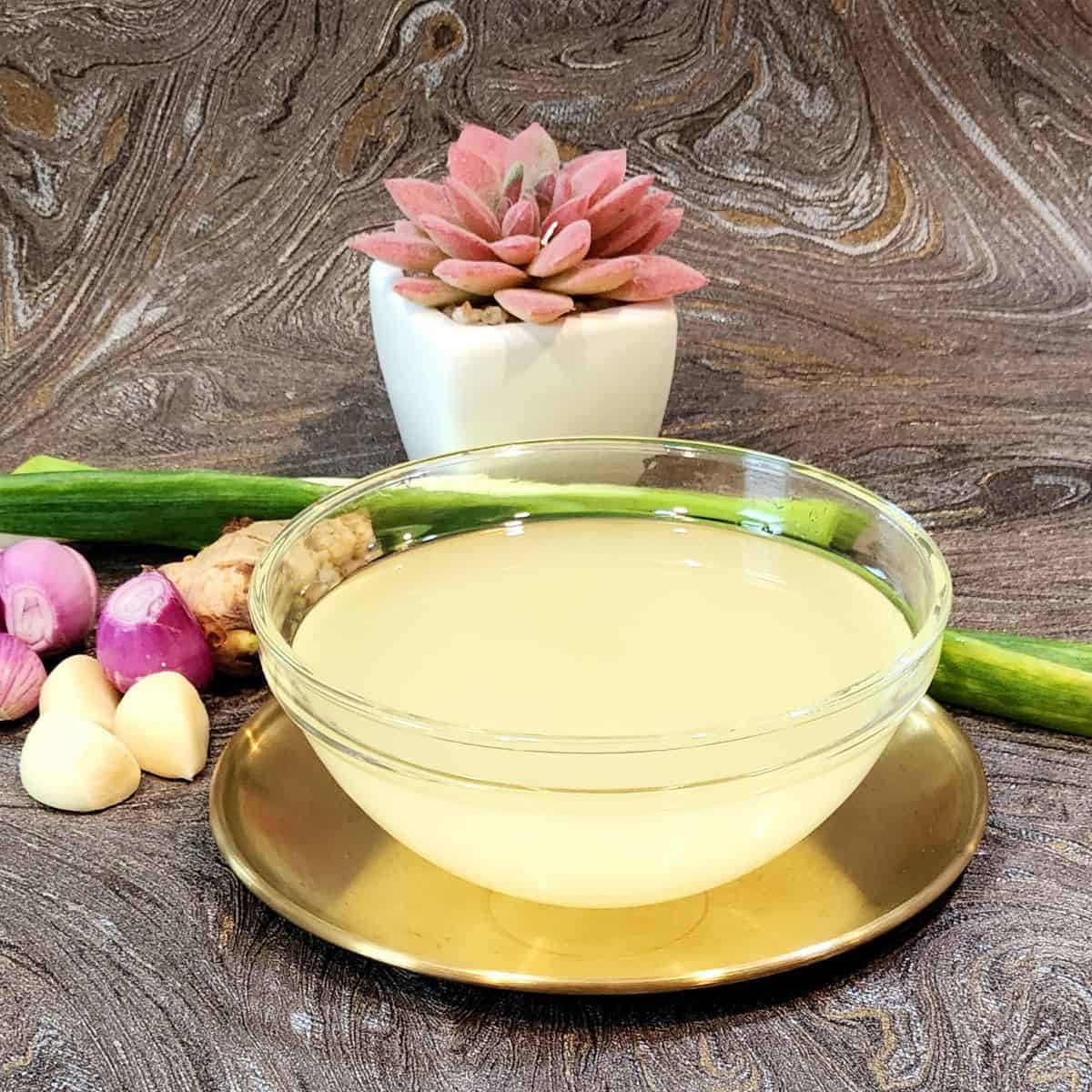 A bowl of Chinese flavored oil with garlic, shallots, ginger, and leeks next to it.