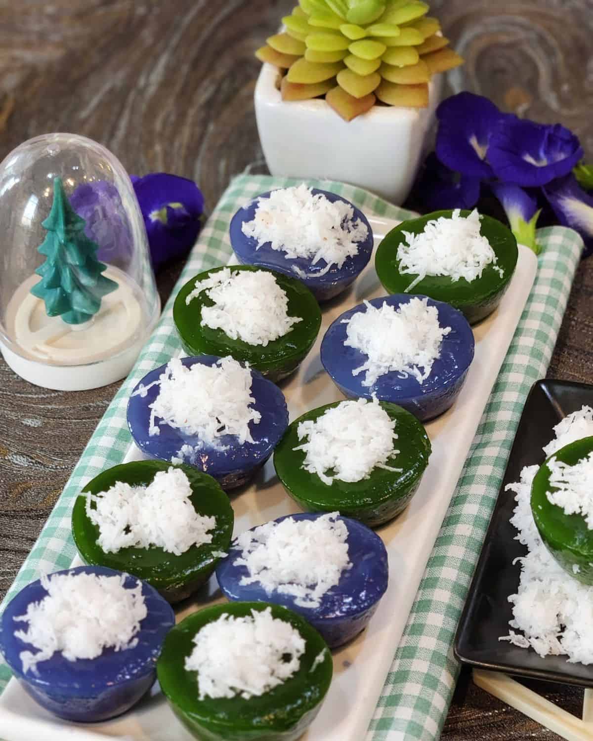 Kuih Kosui pandan and butterfly pea flower on a white rectangular plate with some grated coconut as topping.