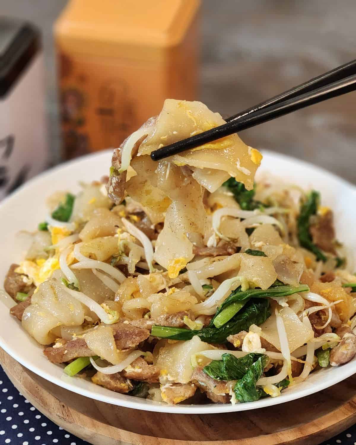 Beef Chow Fun or Kwetiau Goreng on a white plate with black chopsticks.