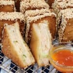 Several pieces of Menbosha - Korean fried shrimp toast in a wooden basket with menbosha sauce next to it.