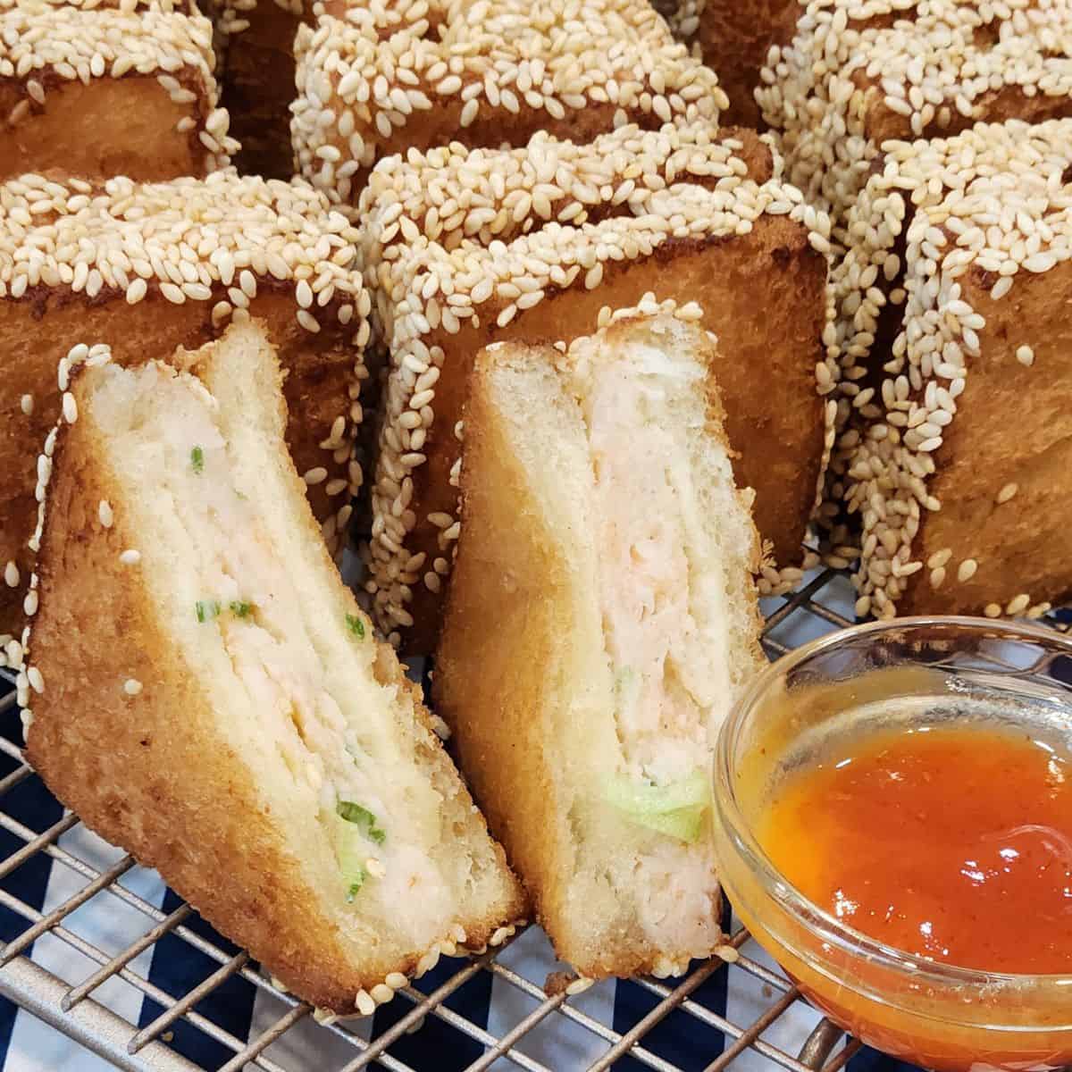 Several pieces of Menbosha - Korean fried shrimp toast in a wooden basket with menbosha sauce next to it.