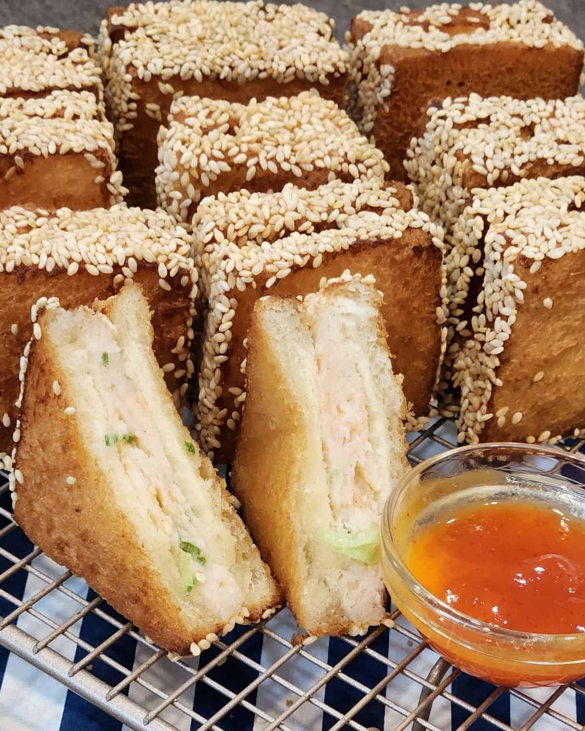 Several pieces of Menbosha - Korean fried shrimp toast in a wooden basket with menbosha sauce next to it.