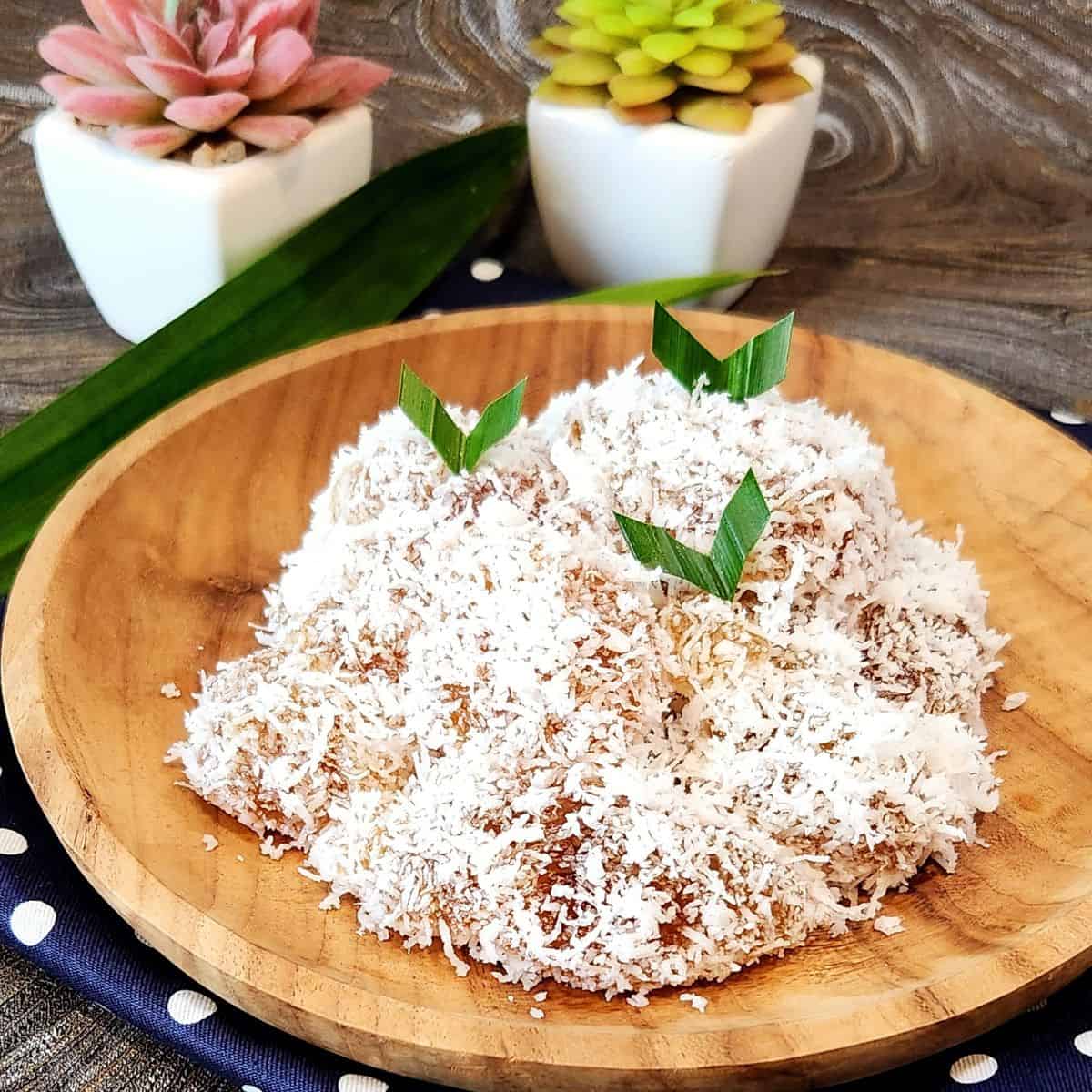 A wooden plate with ongol ongol covered with coconut with pandan leaves as decoration.