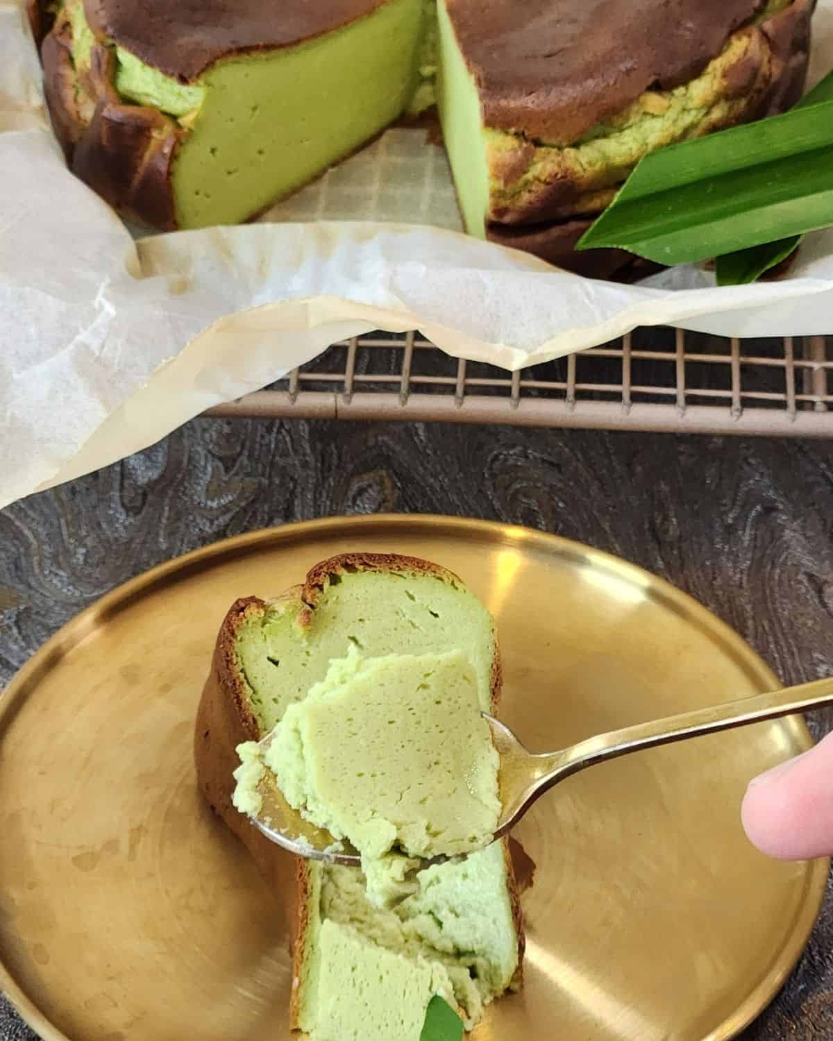 A slice of pandan cheesecake on a golden plate with a small spoon.