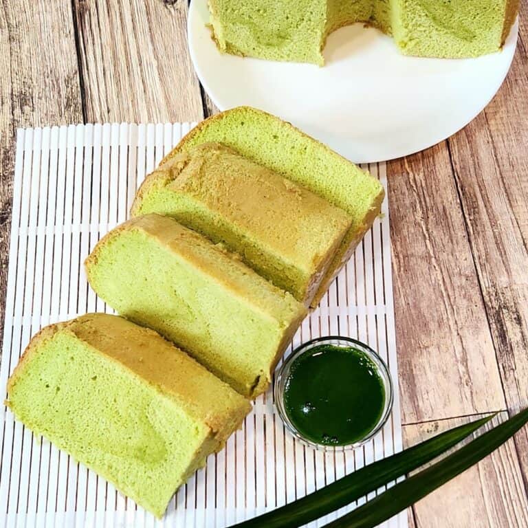 A few slices of pandan chiffon cake on white plastic tray with a cup of pandan extract next to it.