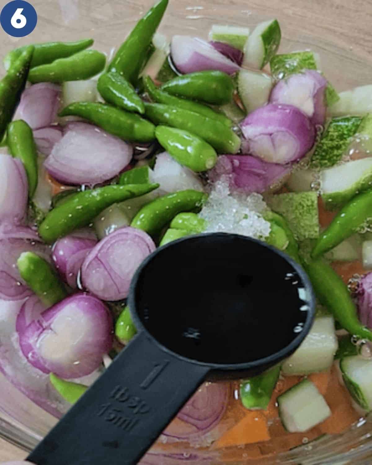A spoon of vinegar is being added to  the cucumbers.