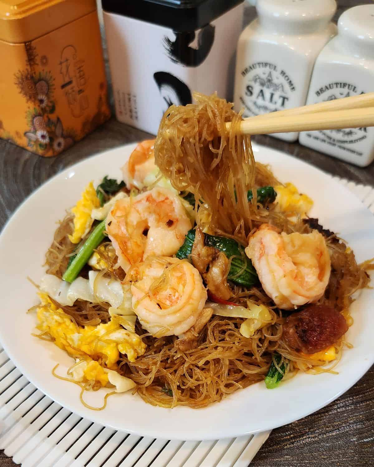 A pair of chopsticks holding shrimp chow mei fun.