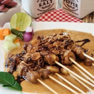 A plate of chicken satay with peanut sauce, pickles, and fried shallots.