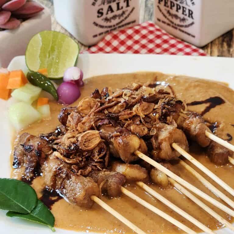 A plate of chicken satay with peanut sauce, pickles, and fried shallots.