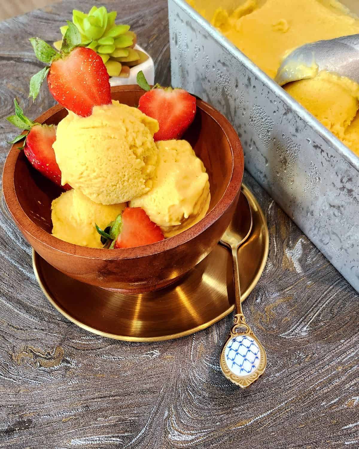 A bowl of mango ice cream with strawberries and a spoon.