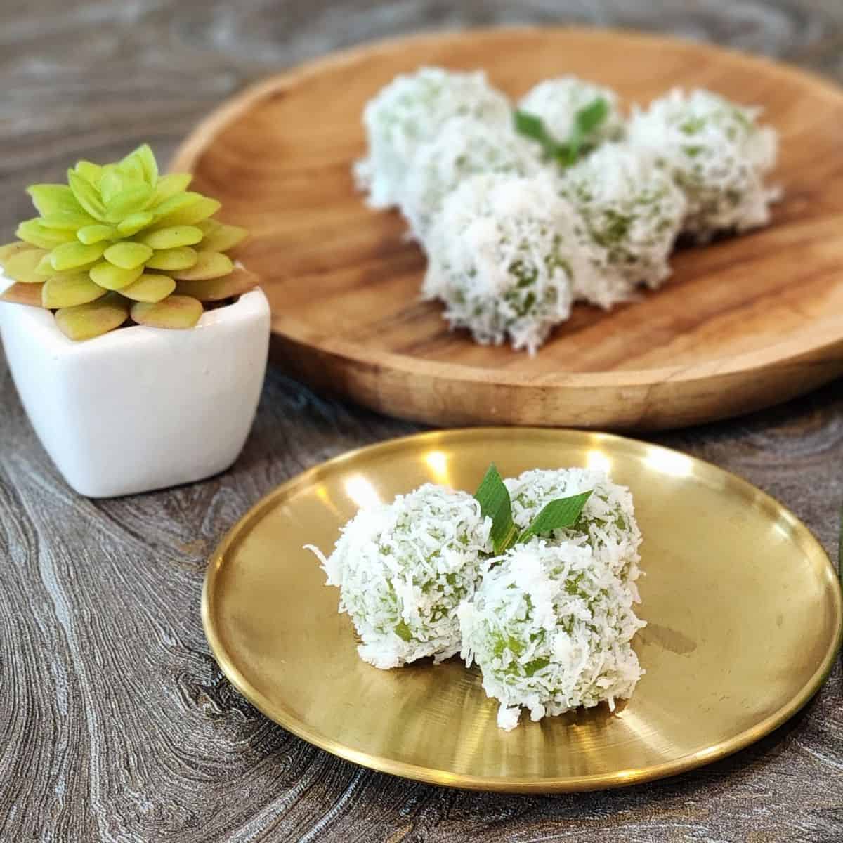 A golden plate with three onde onde and a wooden plate with six klepon.